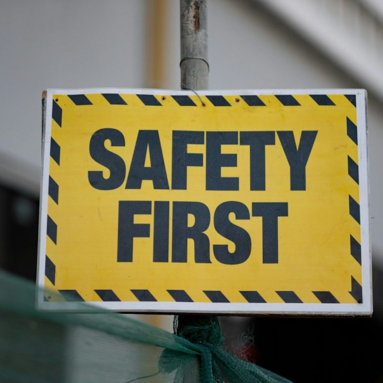 Yellow sign with black text reading "SAFETY FIRST" and caution stripes.