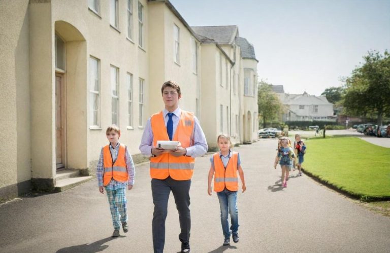 Fire Warden (Edu) A man and two children wearing hi-vis vests walking along a school path.