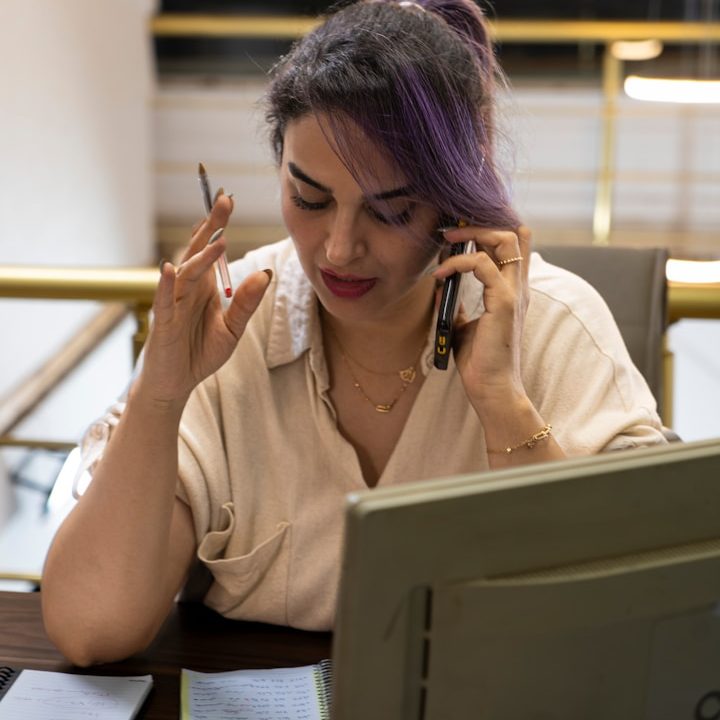 Woman talking on the phone while holding a pen and looking at paperwork.