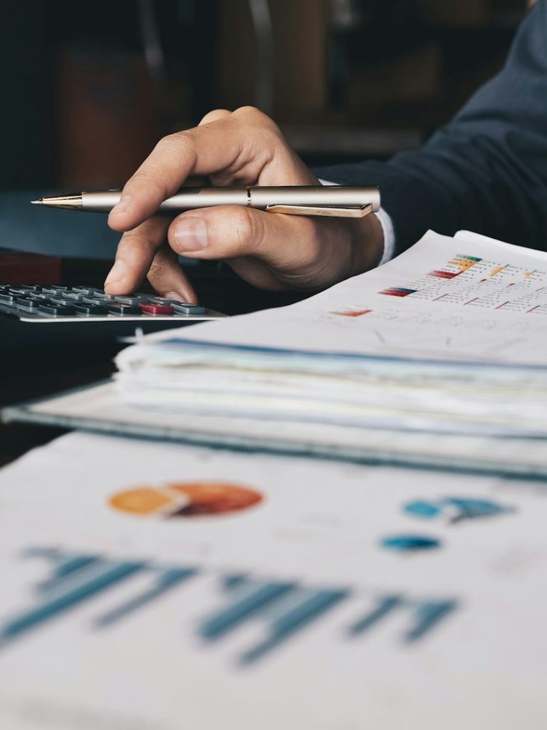 A hand using a calculator, with documents and charts on the table.